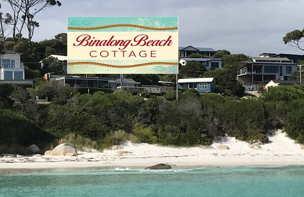 Skilt for Binalong Beach Cottage med udsigt til kysthuse og strand.