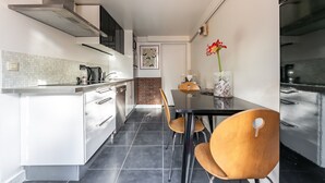 A modern kitchen with white cabinetry, a black countertop, and a dining area with a black table and wooden chairs. - Comfortable studio in a quiet location 10 minutes from the RER station (Joinville le pont)