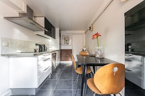 Cozinha moderna com armários brancos, bancada preta e área de refeições com mesa preta e cadeiras de madeira.