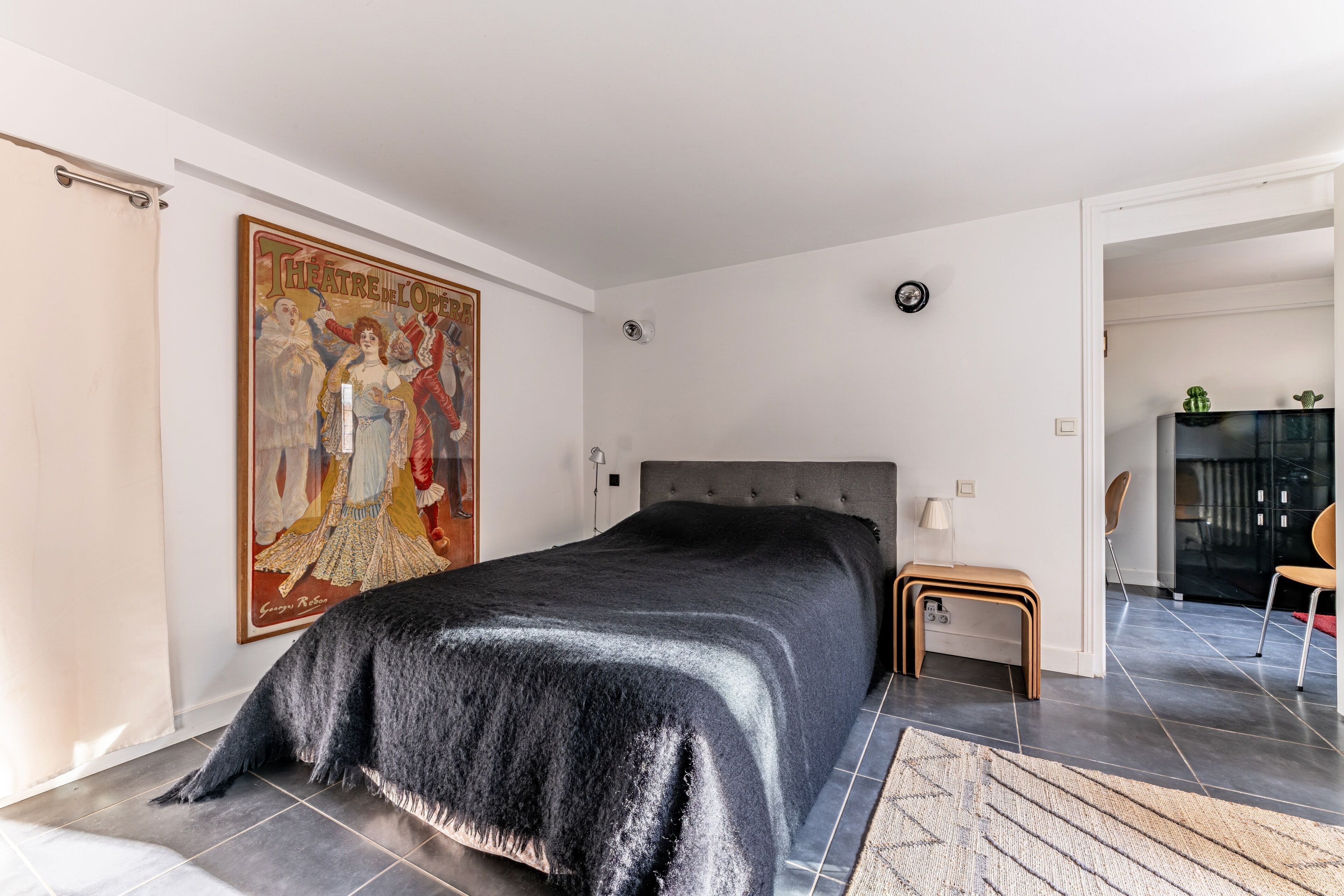 A bedroom with a large bed, a painting on the wall, and a view into another room.