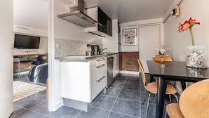 A modern kitchen with white cabinetry, a black countertop, and a dining area with a black table and wooden chairs. - Comfortable studio in a quiet location 10 minutes from the RER station (Joinville le pont)