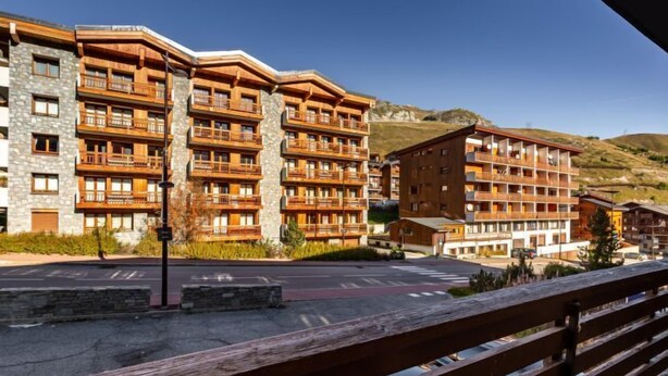 Un hotel a più piani con balconi, facciata in pietra e uno sfondo collinare.