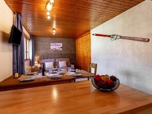 Un coin repas chaleureux avec une table en bois dressée pour deux personnes, un saladier rempli de fruits et une paire de skis accrochés au mur.