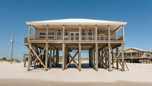Una casa sulla spiaggia in legno con un balcone, costruita su palafitte sulla sabbia.