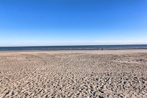 Ein breiter, sandiger Strand mit deutlichen Spurren und einem wolkenlosen, blauen Himmel.