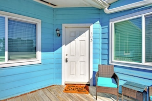 Welcome to a charming home with a cozy porch featuring a white door, two windows, and a comfortable wicker chair.