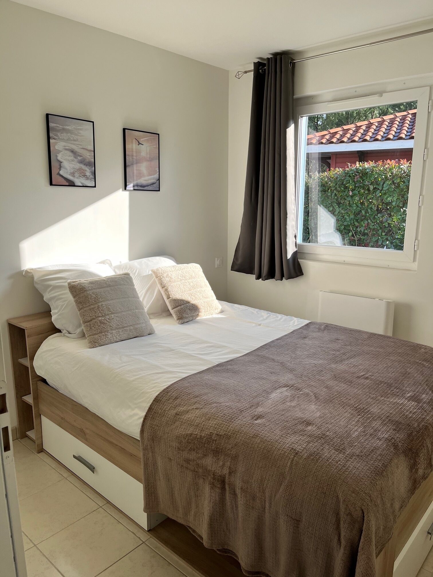 A bedroom with a bed, a window with curtains, and two framed pictures on the wall.