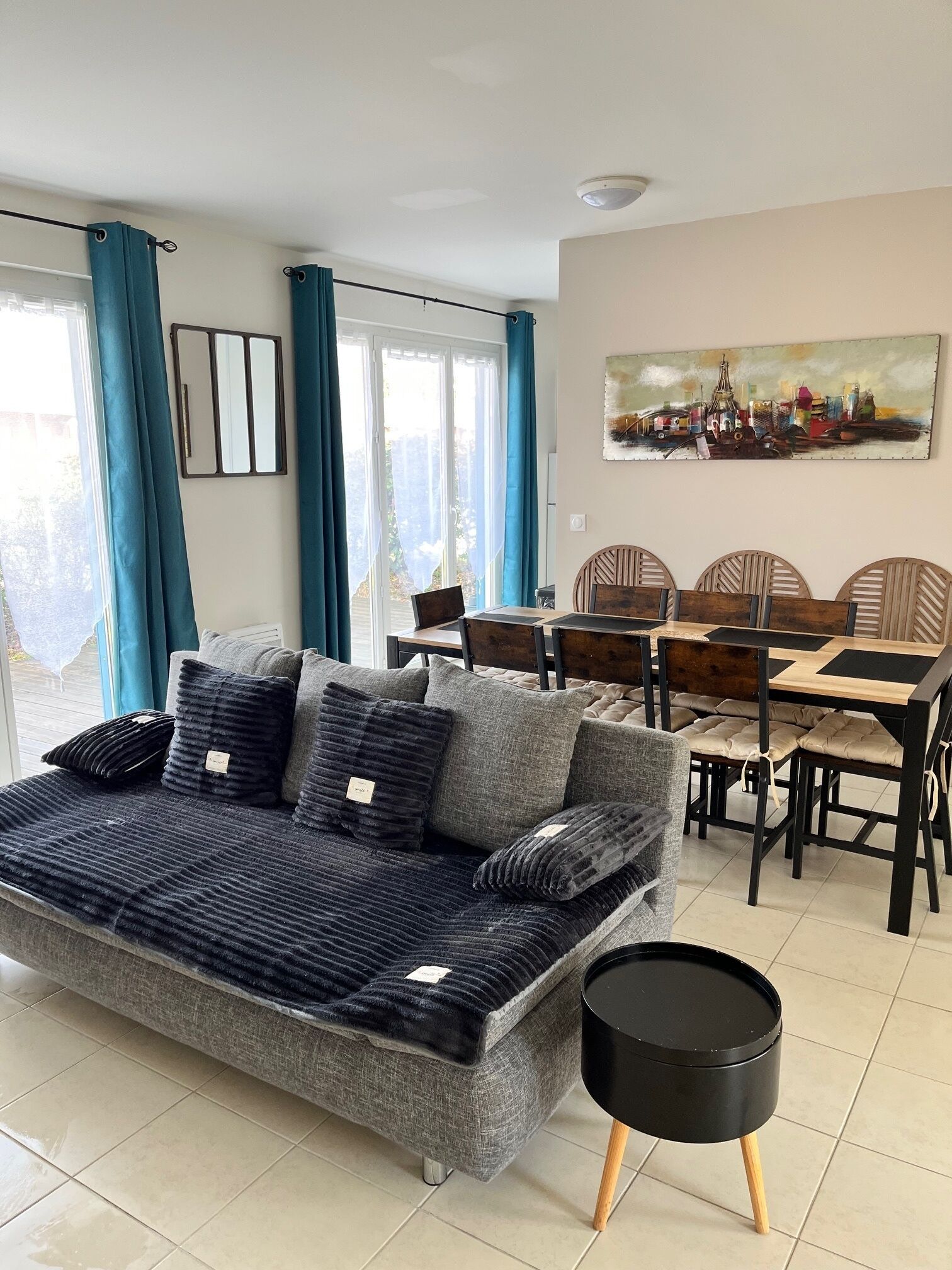 A modern living room with a sofa, dining table, chairs, and a painting on the wall.