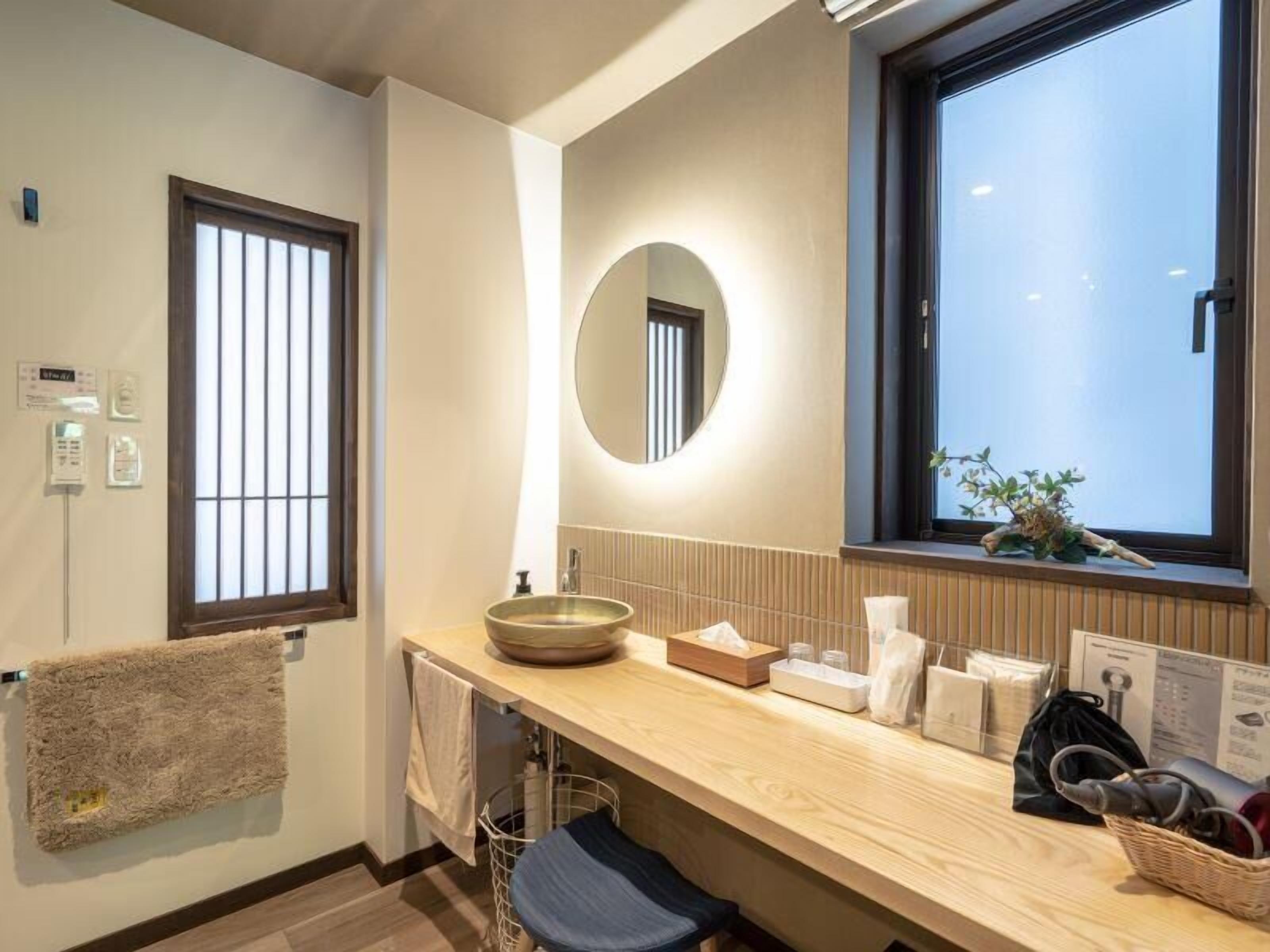 Ein modernes Badezimmer mit einem Holzwaschtisch, einem runden Spiegel, einem Fenster mit Ausblick und einem Handtuchhalter.