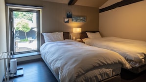 Een hotelkamer met twee bedden, een raam met uitzicht op de omgeving, een airconditioner en een klein tafeltje met een lamp.