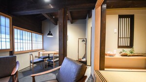 Een traditionele Japanse kamer met tatami vloerbedekking, een lage tafel en een zithoek met kussens en een houten stoel.