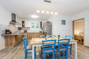 Una cocina compacta con zona de comedor, que incluye una mesa de madera y sillas azules, un horno empotrado y un refrigerador.
