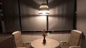 Et rundt bord med hvid dug, omgivet af to hvide, polstrede stole. En dekorativ vase med en blomst står på bordet.