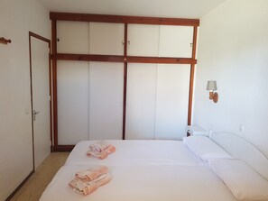 A bedroom with a bed, two towels, a wardrobe, and a wall-mounted lamp.