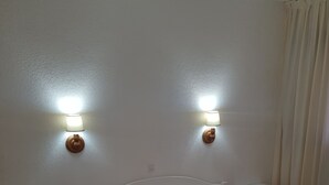 Et hotelværelse med en enkeltseng, to sengeborde, et natbord og en lampe fastgjort til væggen.