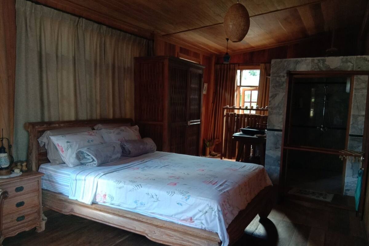 Una cama con estructura de madera y ropa de cama floral en una habitación con paredes de madera y una chimenea de piedra.
