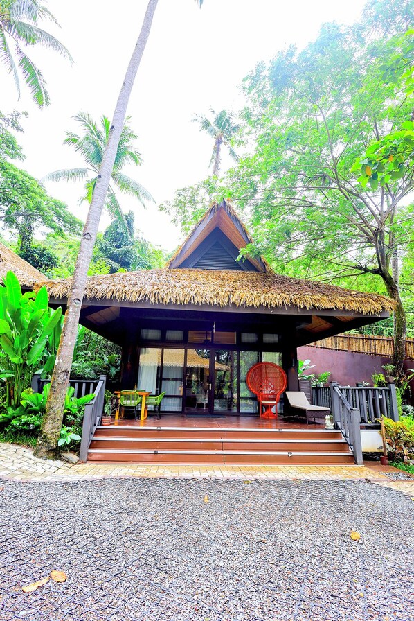A thatched-roof structure with a staircase leading to an entrance, surrounded by tropical vegetation. - Lihim Resorts (El Nido)