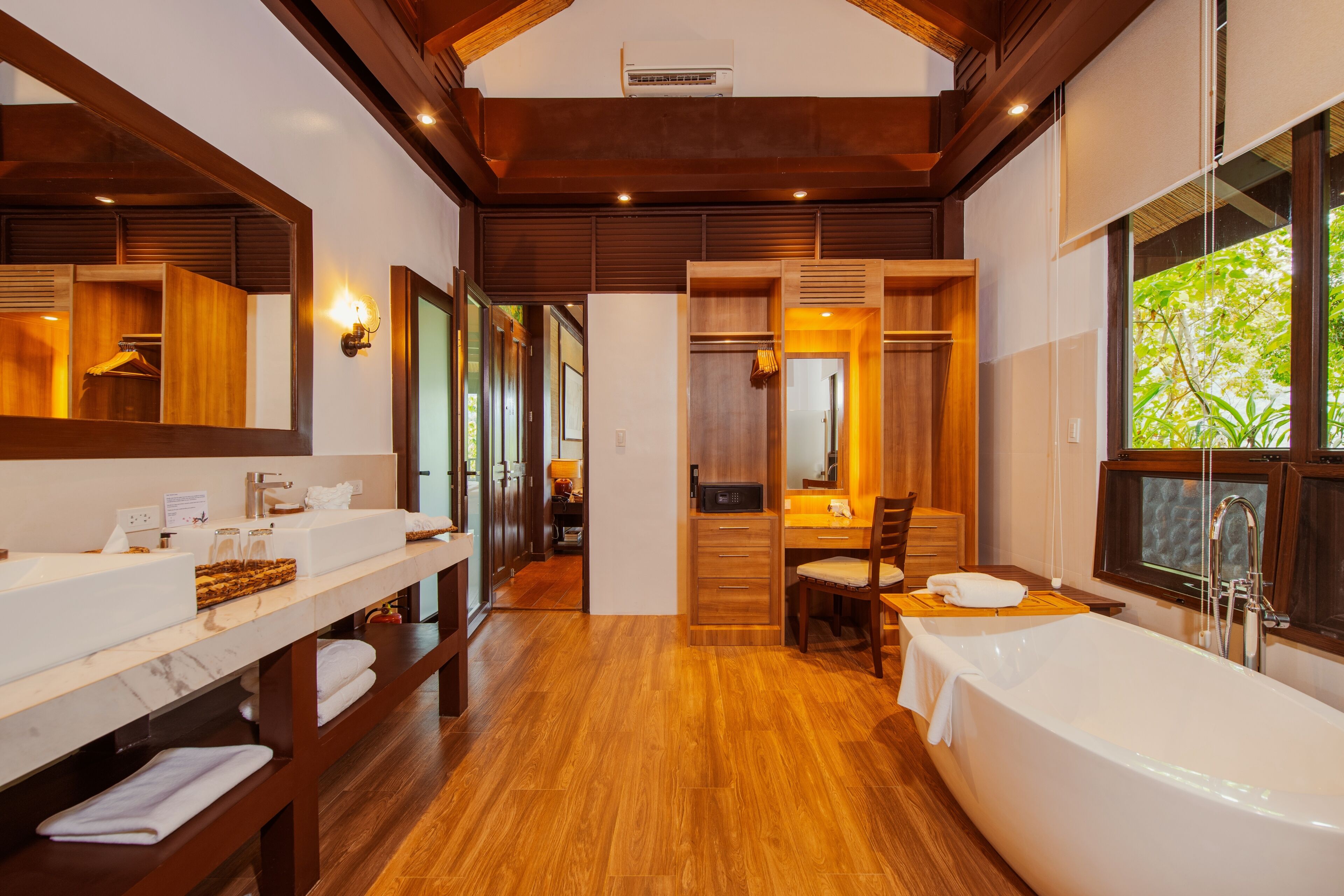 A modern bathroom with a large bathtub, two sinks, a vanity, and a wooden floor.