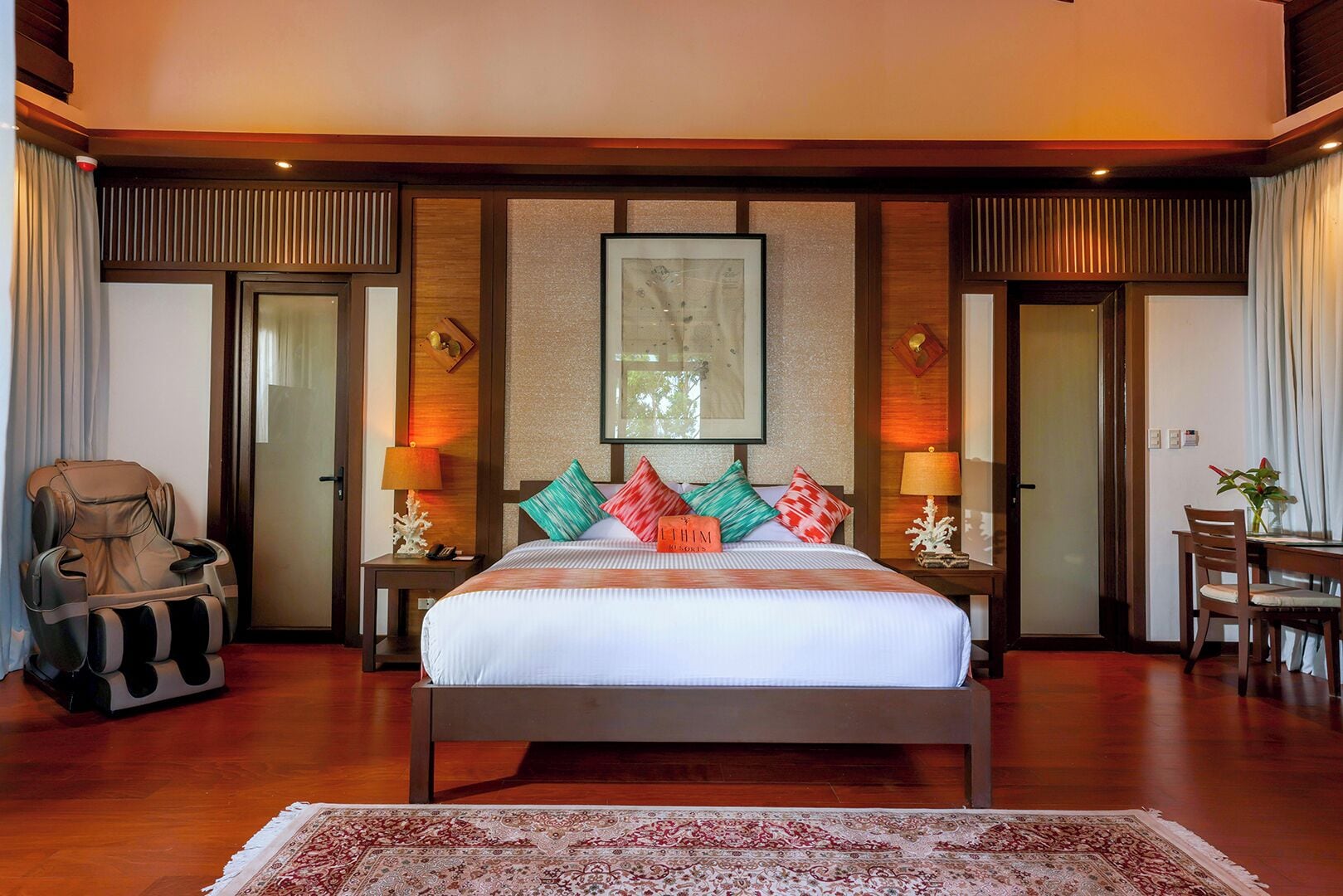 A spacious bedroom with a large bed, a massage chair, a dining table, and a framed picture on the wall.