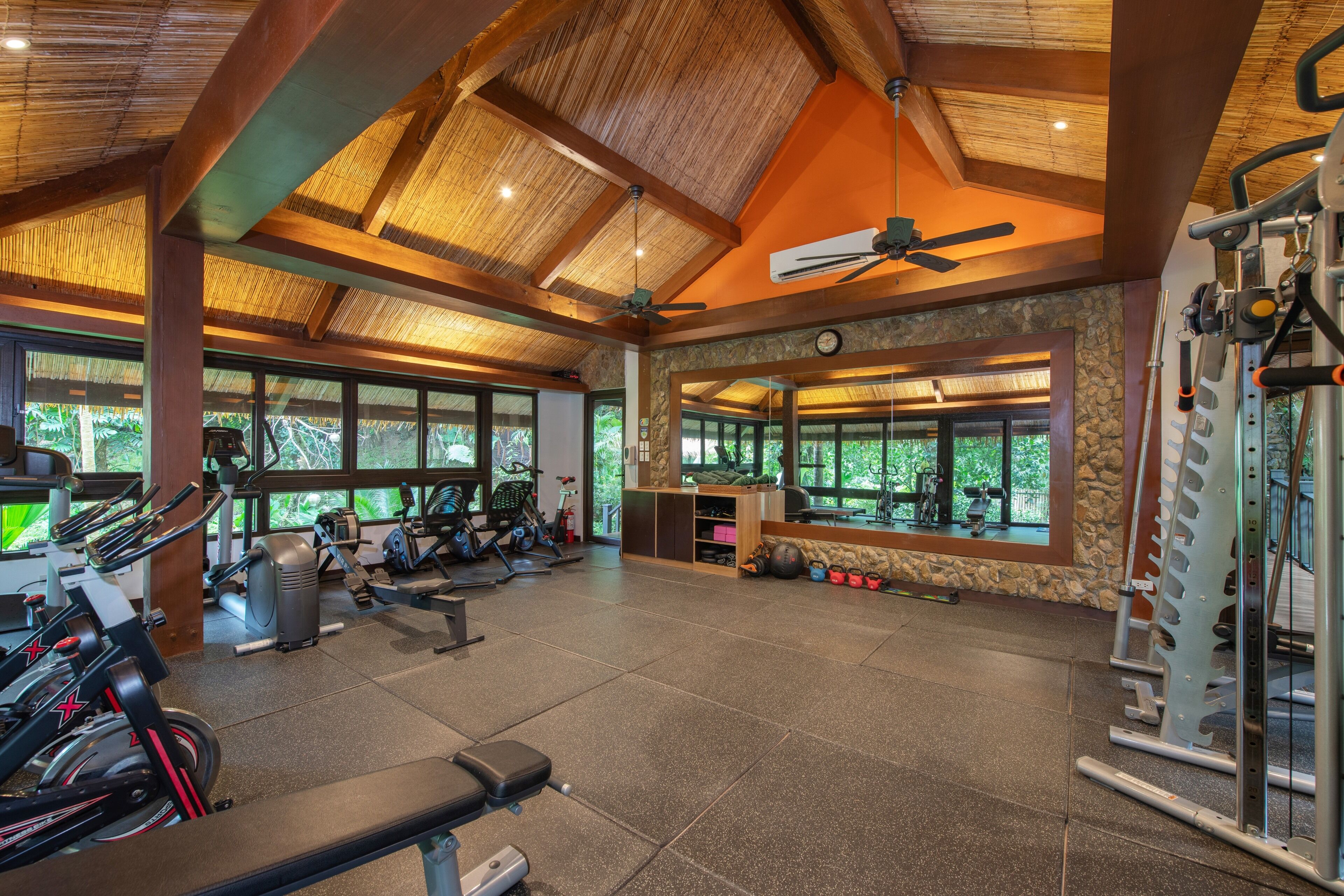 A gym with exercise equipment, large windows, and a wooden ceiling.