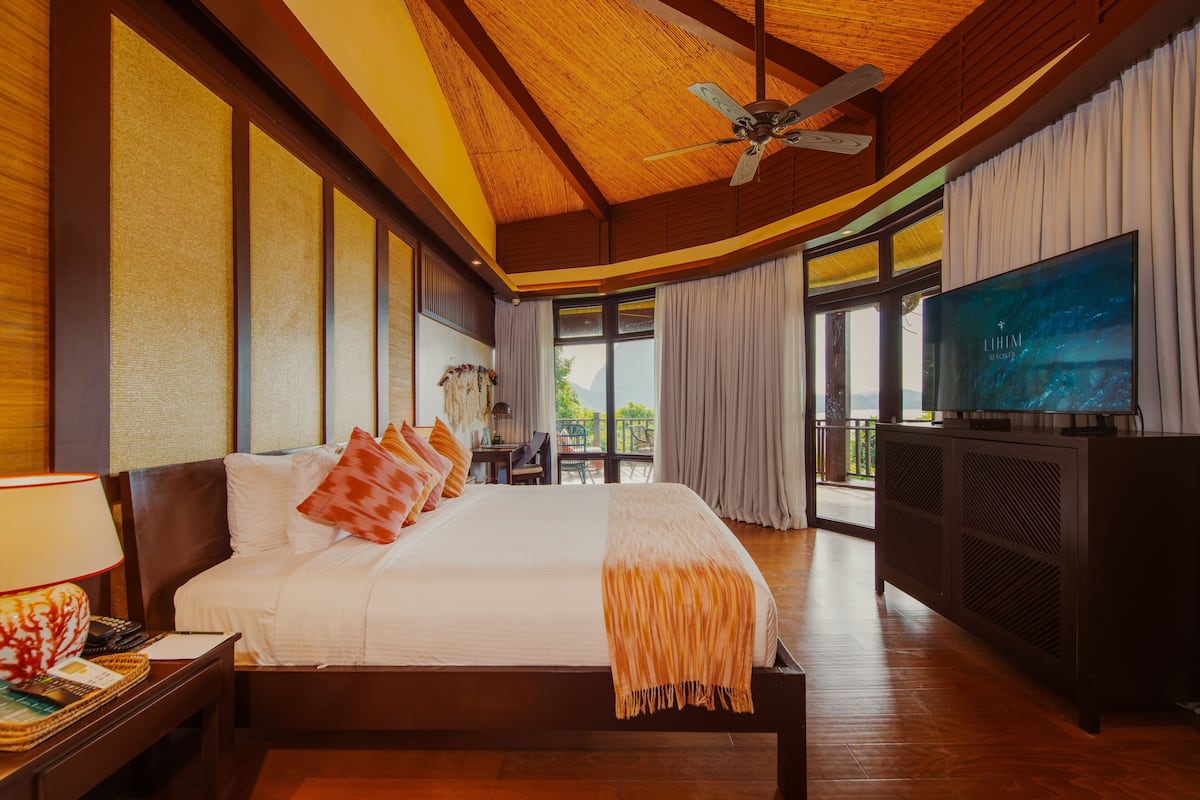 A spacious bedroom with a large bed, a television, and a balcony with a view.