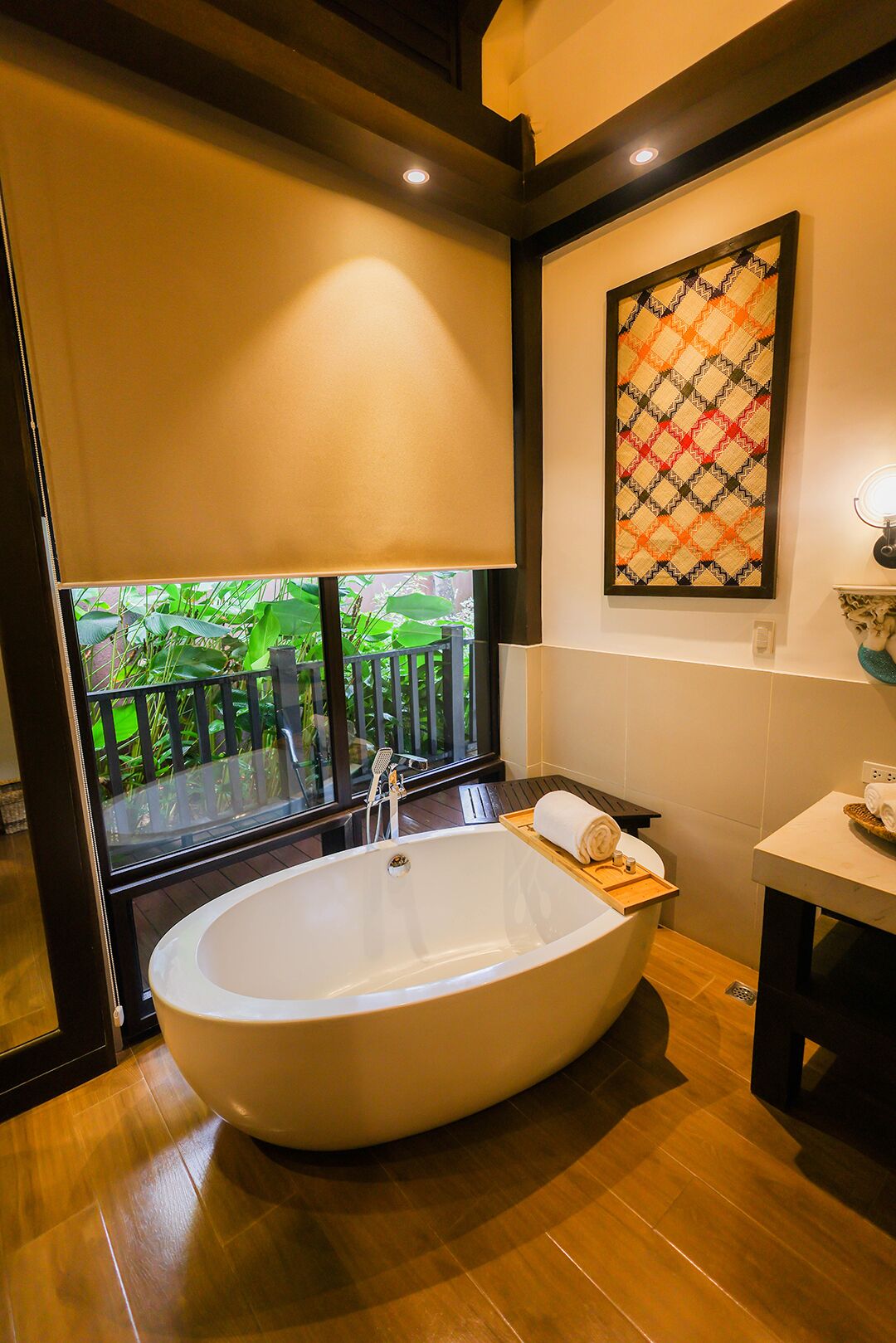 A modern bathroom with a freestanding bathtub, a window with a view of greenery, and a wall-mounted towel rack.
