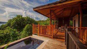 Una terraza de madera con piscina, rodeada de abundante vegetación y con vistas a un cuerpo de agua.