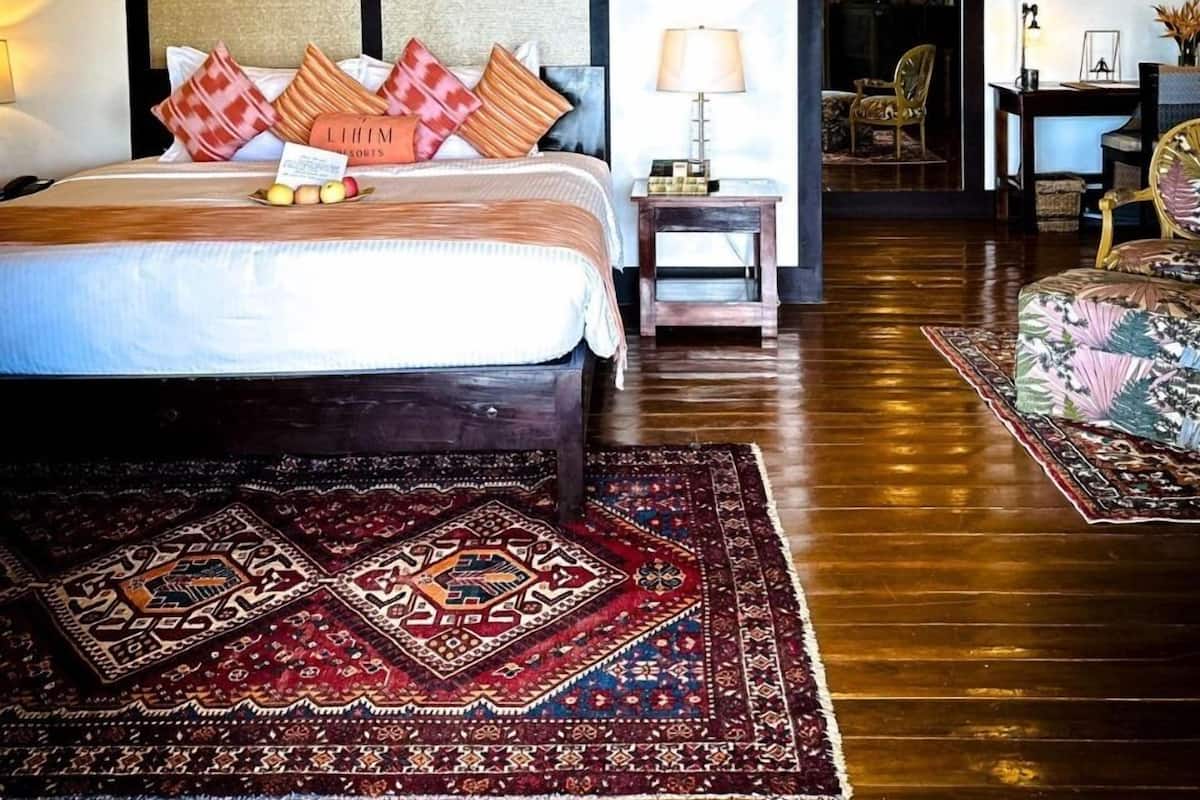 A bedroom with a large bed, a nightstand, a lamp, a chair, and a view of the outside.