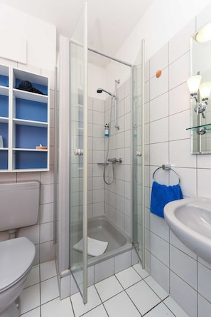A bathroom with a glass-enclosed shower, a toilet, a sink, and a blue towel rack.
