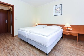A hotel room with a double bed, wooden floor, two bedside tables with lamps, and a wall-mounted picture.