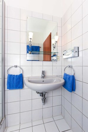 A bathroom with white tiled walls, a white sink with chrome fixtures, and two blue towels hanging on towel rings.
