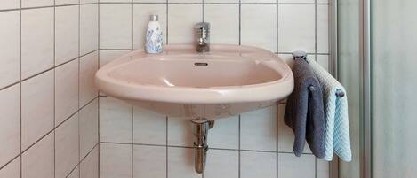 A bathroom with a sink, mirror, towel rack, and shower.