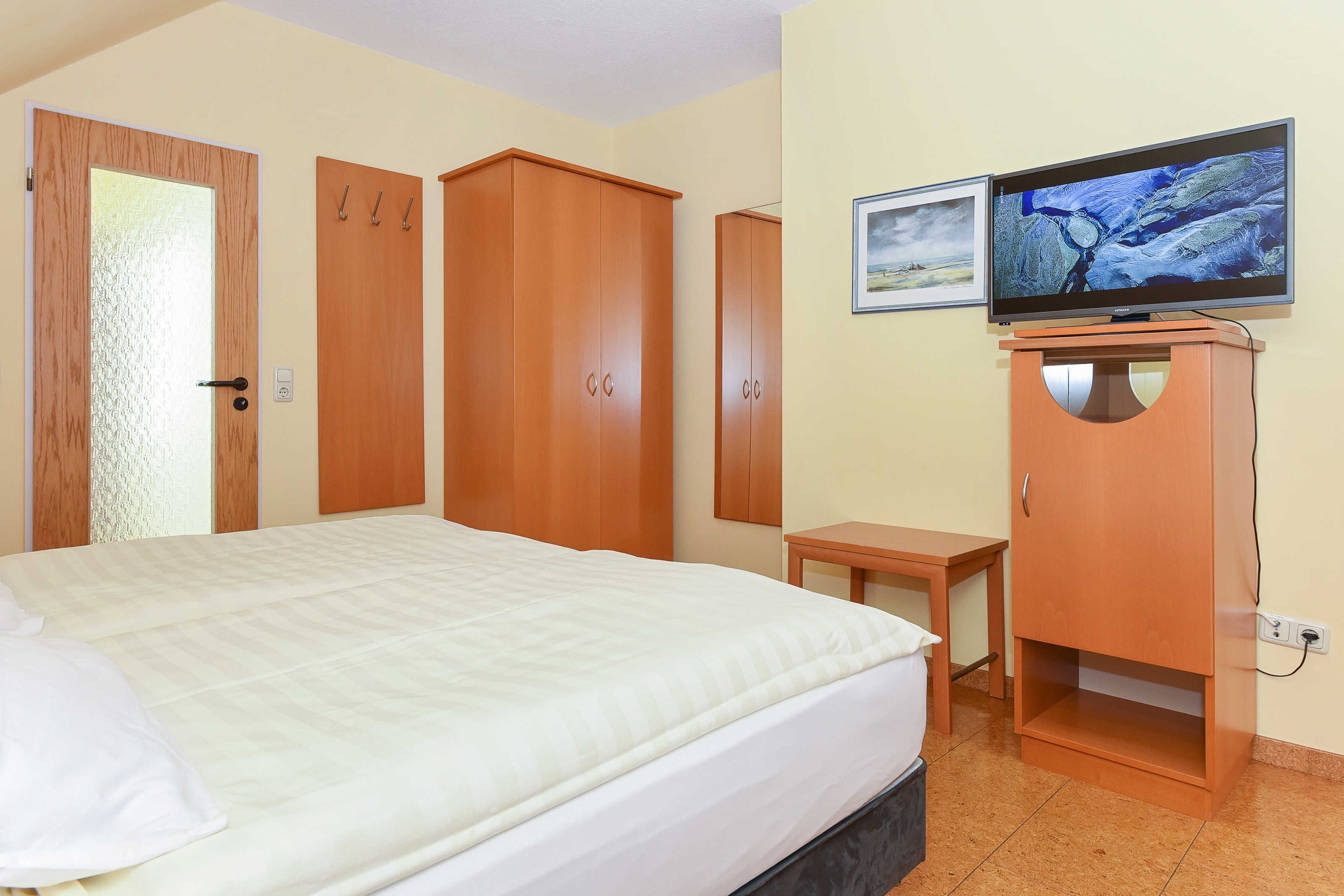 A hotel room with a bed, wooden wardrobe, a television, and a small table.