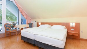 Ein Schlafzimmer mit einem großen Bett, einem kleinen Tisch, einem Stuhl und einem Fenster mit Vorhängen.