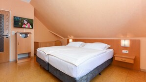 Une chambre à coucher avec un lit, un téléviseur fixé au mur, une armoire en bois et une table de chevet avec une lampe.