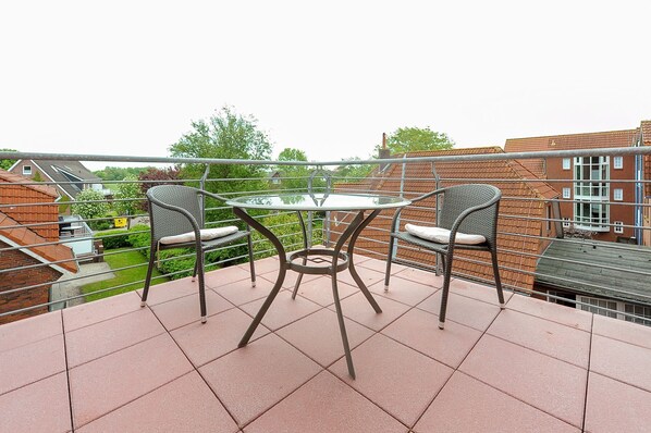 A balcony with a glass table and two wicker chairs, surrounded by a metal railing.
