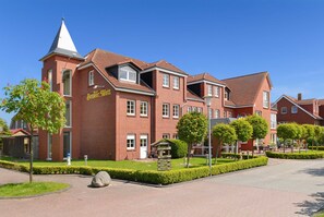 A red-brick hotel with a tower, a signboard, and a well-maintained garden.