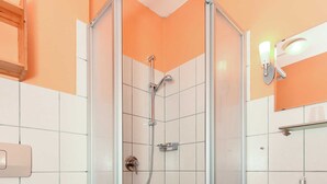 Une salle de bain avec une douche à parois de verre, des toilettes, un lavabo et une poubelle.