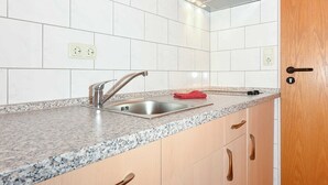 A kitchen with white tiled backsplash, granite countertop, stainless steel sink, wooden cabinets, and a wooden door. - Double room Krabbe in the Hotel-Pension Altes Siel - Double room Krabbe with (Esens)
