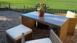 A wicker outdoor seating area with a glass-top table, cushions, and a potted plant. - Kleine Ferienwohnung (Gelting)