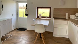 A compact kitchen with a window, a white chair, and a wooden floor. - Kleine Ferienwohnung (Gelting)