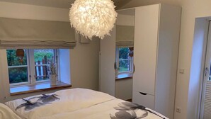 A bedroom with a bed, a large mirror, and a window with a view of greenery. - Kleine Ferienwohnung (Gelting)