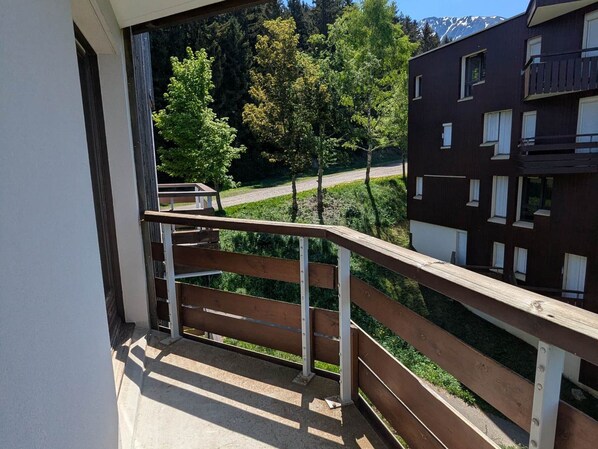 A balcony with a view of a road and trees, a building with multiple windows, and a clear sky.