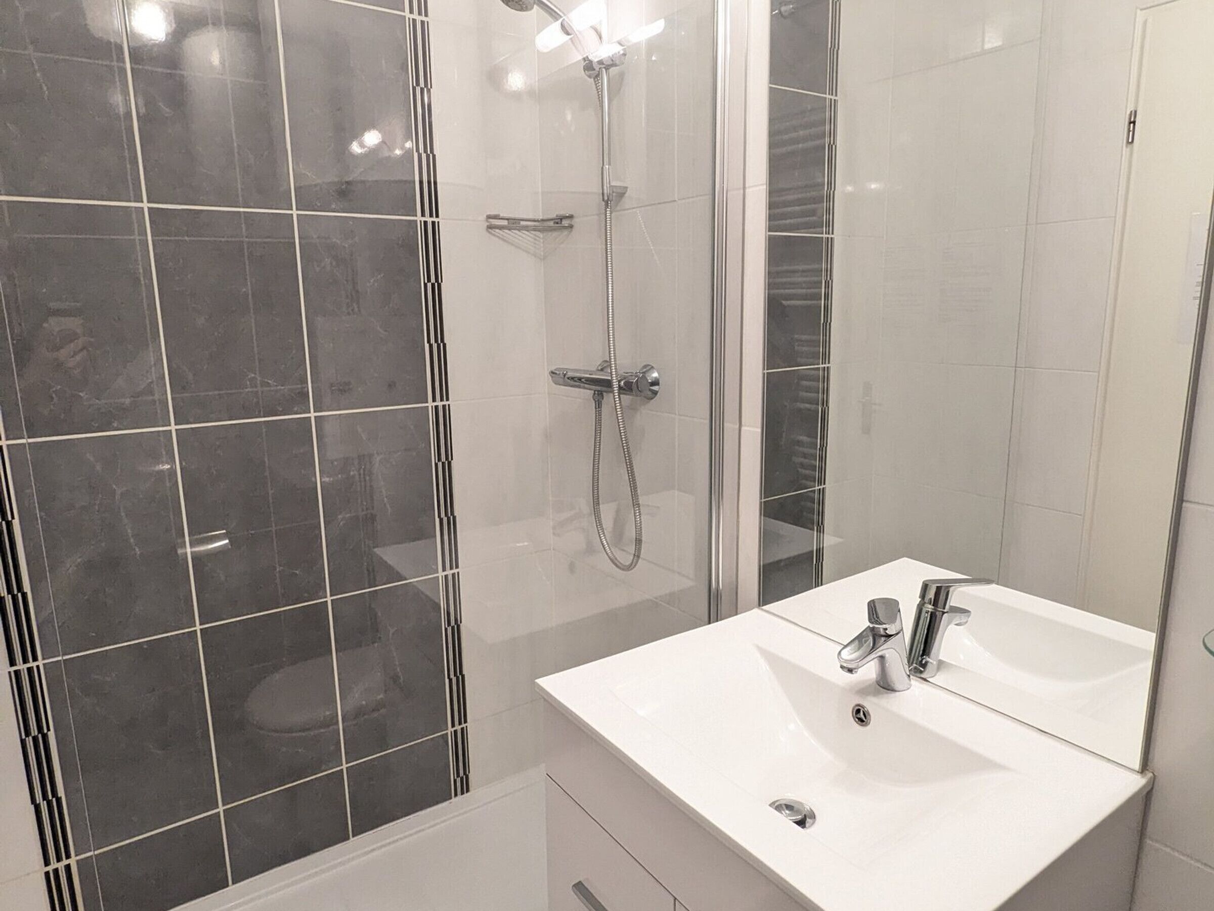 A bathroom with a glass-enclosed shower, a white sink, and a mirror.