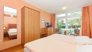 Een hotelkamer met een groot bed, een kledingkast, een bureau met een televisie en een raam met gordijnen.