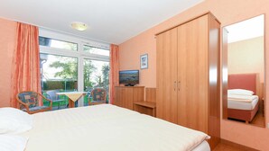 Un dormitorio con una cama, televisor, armario de madera, una mesita y una silla.