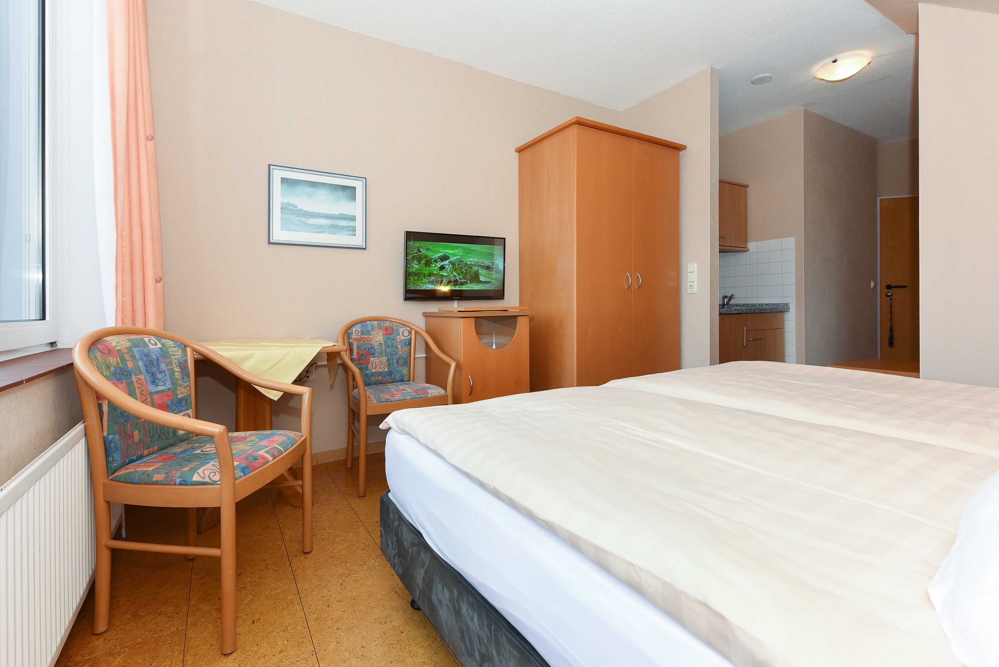 Ein Hotelzimmer mit Bett, zwei Stühlen, einem Fernseher, einem Kleiderschrank und einer kleinen Küchenzeile.