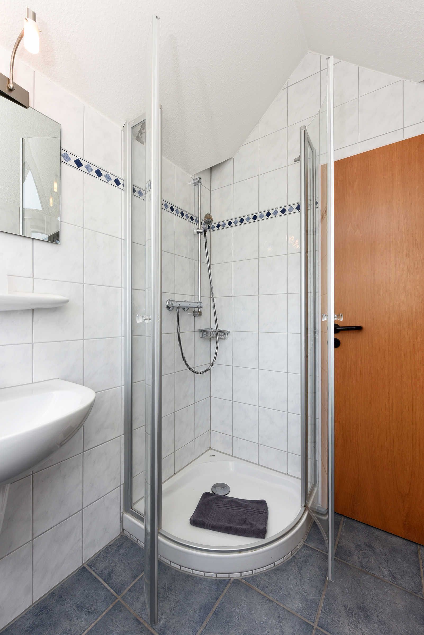 A shower with a glass door, a white sink, and a wooden door in a bathroom.