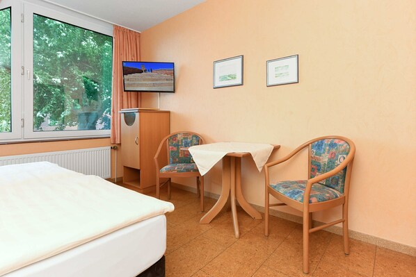 Une chambre d’hôtel avec un lit, une petite table, deux chaises, un téléviseur et des tableaux encadrés au mur.