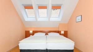 Ein Zimmer mit einem Doppelbett, zwei Dachfenstern und zwei Wandleuchten.